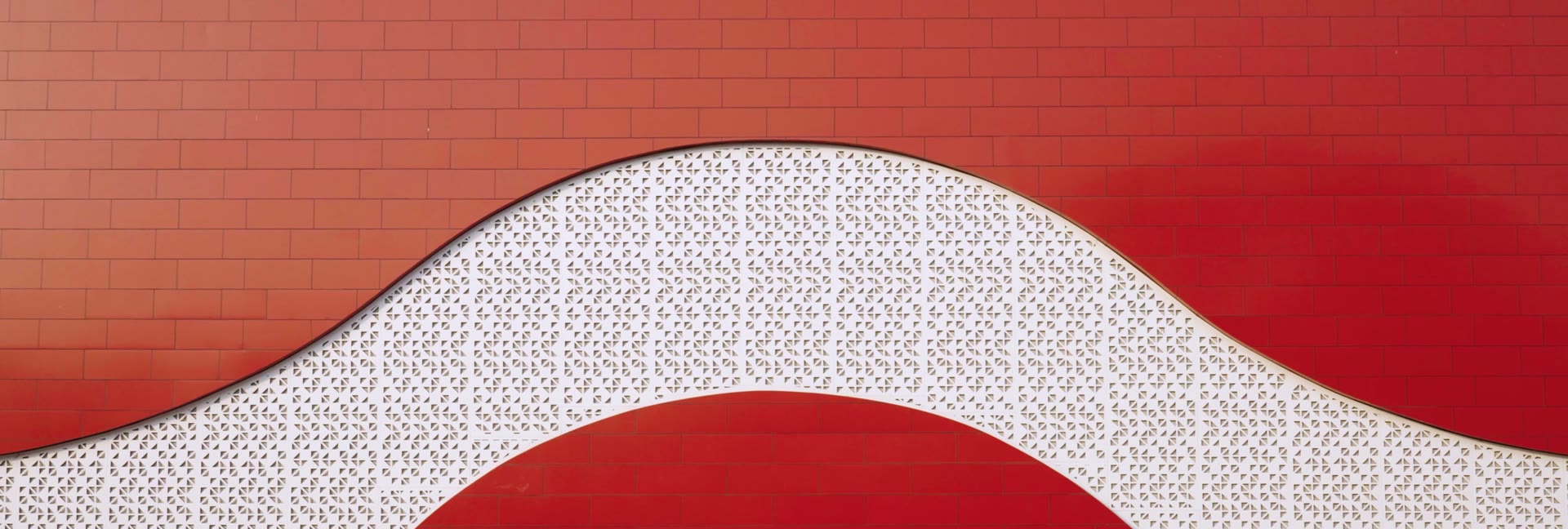 A wavy white perforated screen on the red entrance wall at Rayanapadu